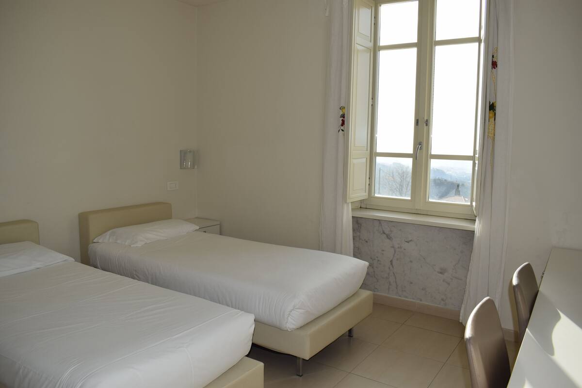 Una habitación con dos camas, un ventanal con vistas y una pared de mármol.