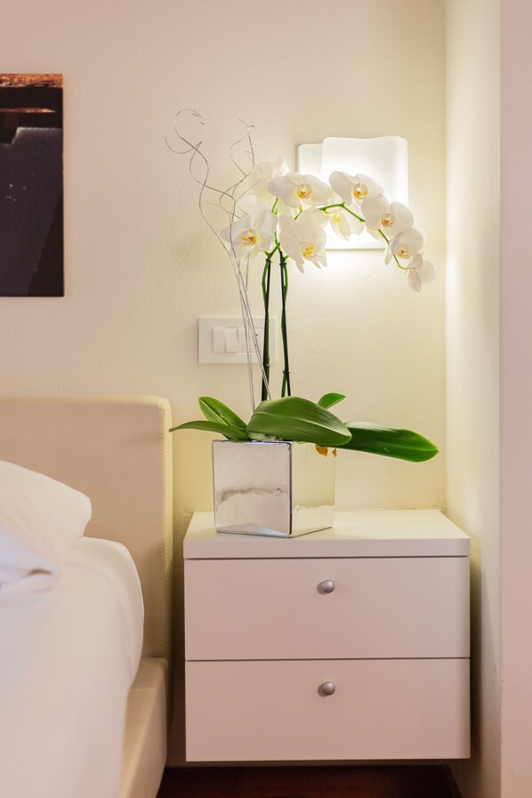 A white bedside table with a vase of white orchids and a small potted plant. - Albergo la Castellana (Fosdinovo)