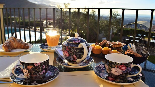 Frühstücksaufstellung mit Croissants, Gebäck und einem Teekessel auf einem Balkon mit Blick auf eine schöne Aussicht.