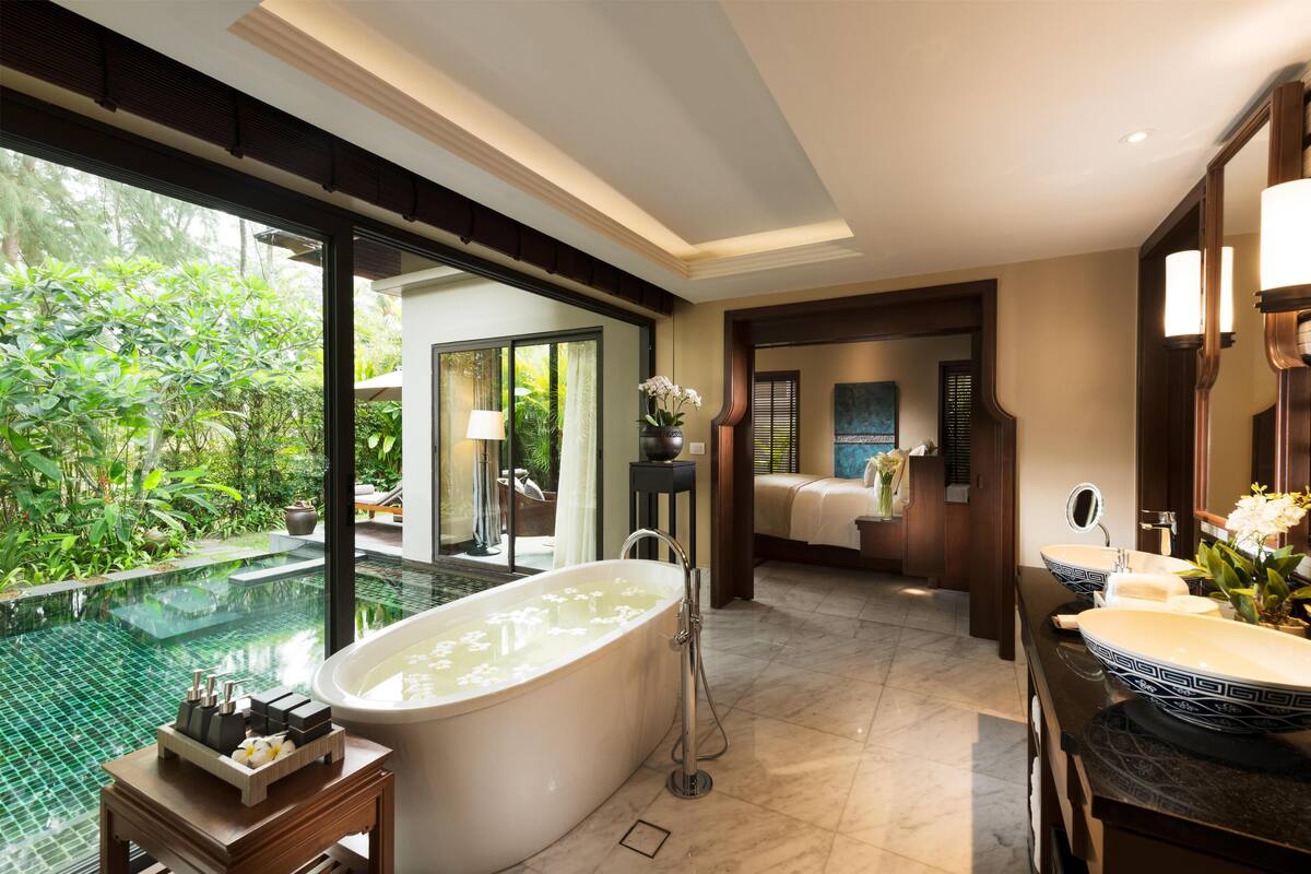 A modern bathroom with a large bathtub, a sink, and a shower. There is a view of a pool outside.