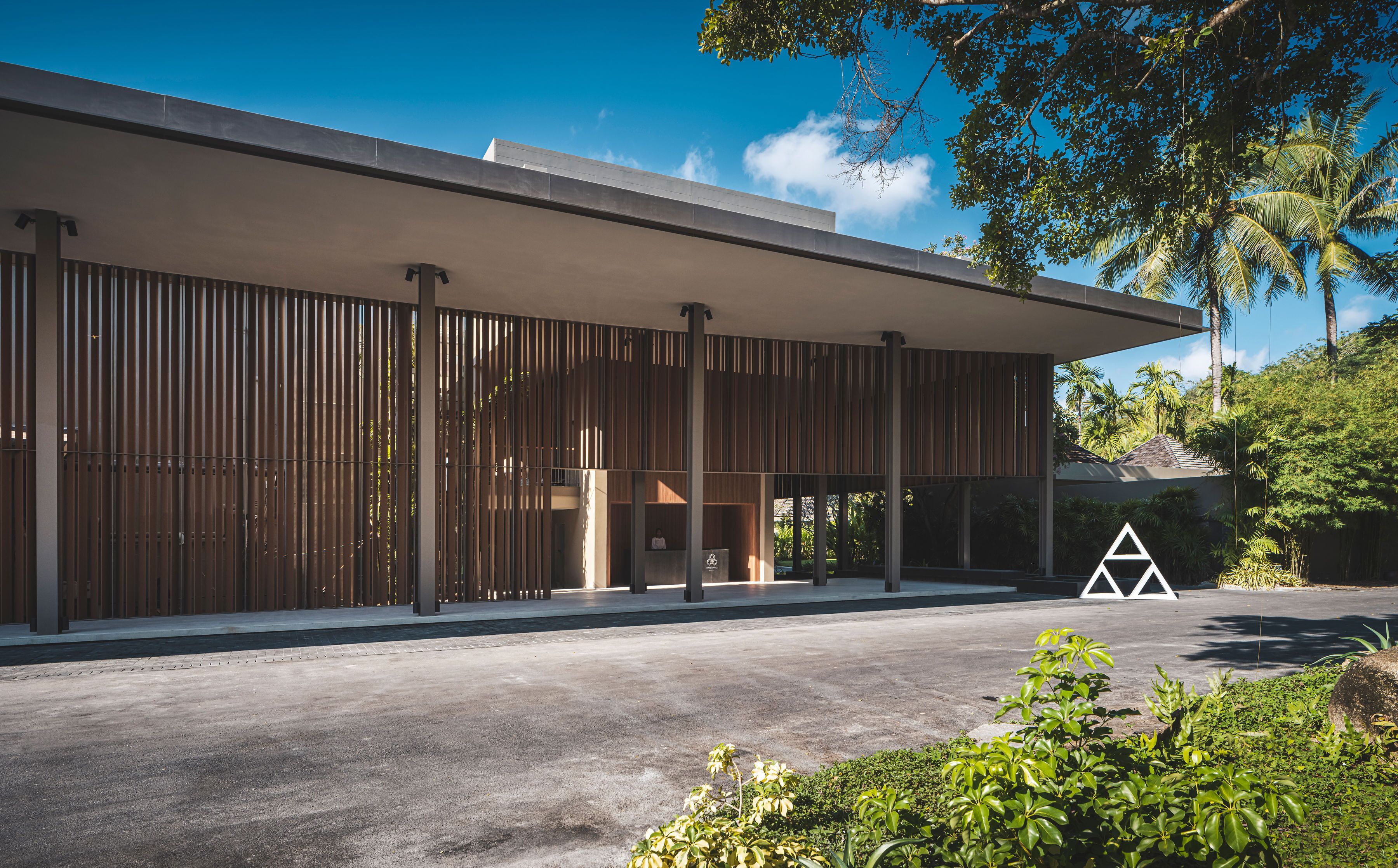 Un edificio moderno con vestíbulo cubierto, listones verticales de madera y suelo de hormigón.