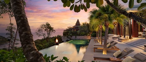A poolside area with lounge chairs and a view of the ocean at sunset.