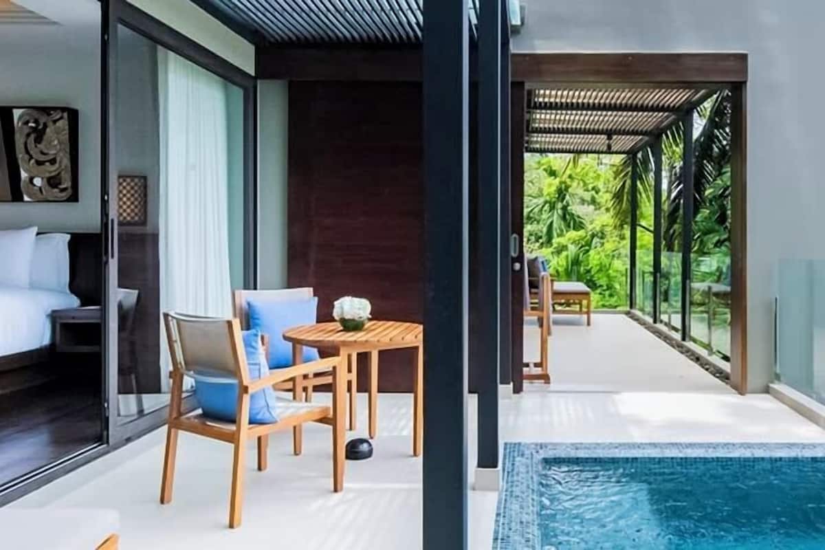A modern hotel room with a bed, a small table with chairs, and a view of a pool.