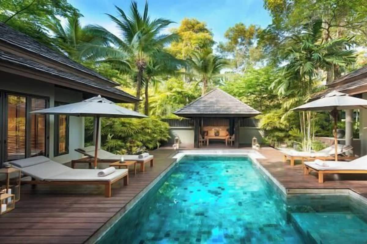 A pool area with lounge chairs and umbrellas, surrounded by lush greenery and tropical trees.