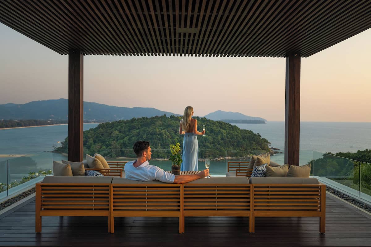 A couple on a wooden deck overlooking a scenic ocean view with mountains in the background.