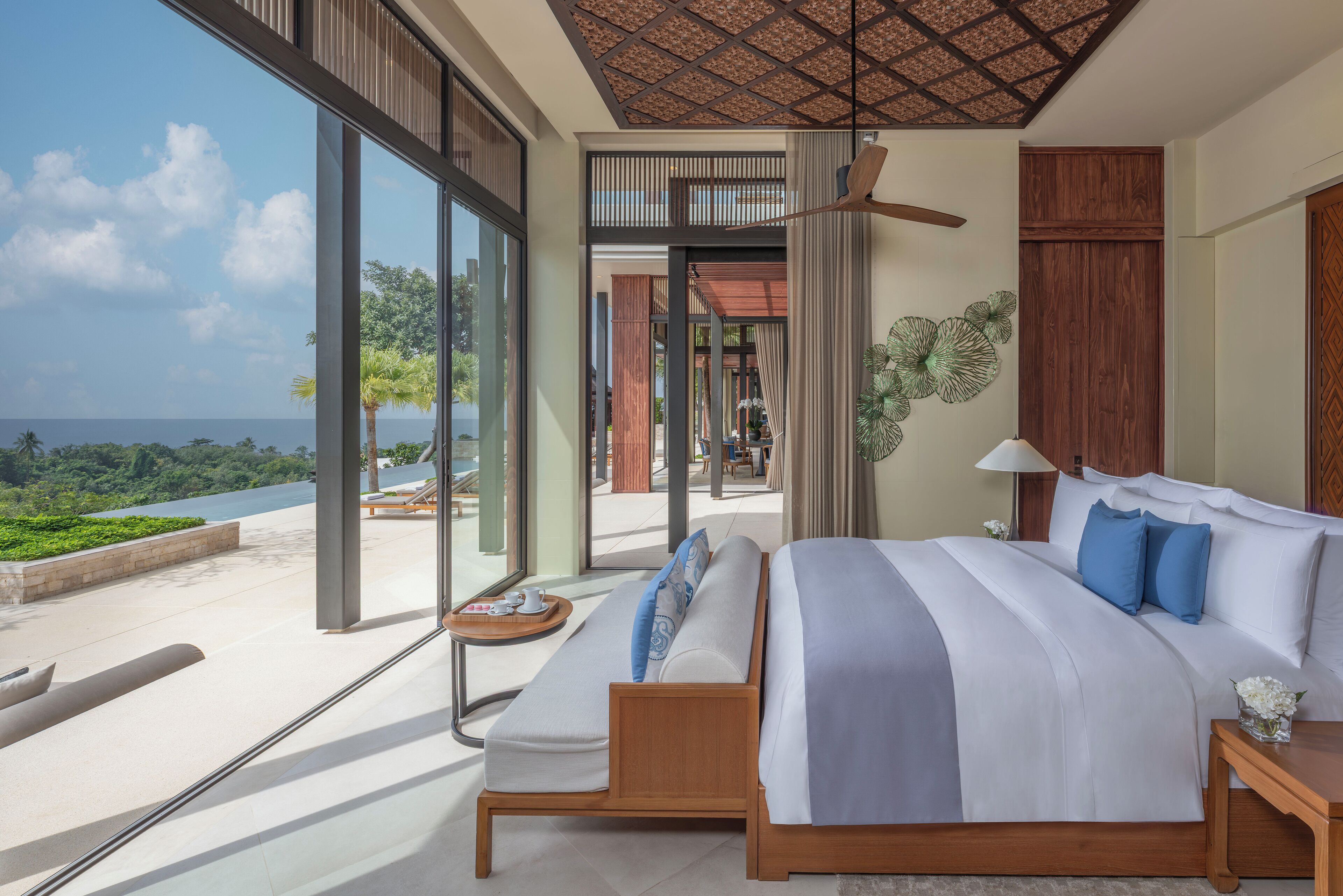 A modern bedroom with a large bed, a ceiling fan, and a view of the ocean.