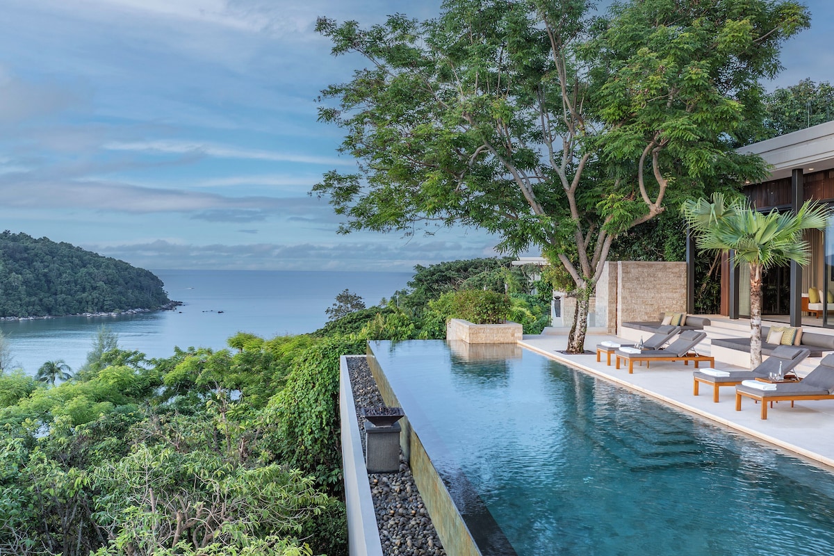 A infinity pool with lounge chairs, a view of the sea, and lush greenery.