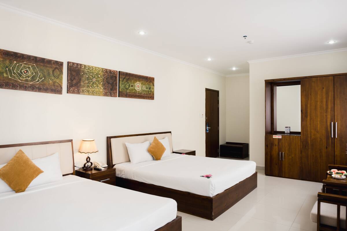 Habitación de hotel con dos camas, un armario de madera, un escritorio con silla y una obra de arte en la pared.