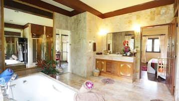 A spacious bathroom with a large bathtub, a wooden vanity, and a mirror above the sink.