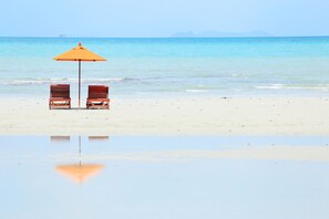 Two wooden chairs and an orange umbrella on a sandy beach with calm water and distant mountains. - Viva Vacation Resort (Koh Samui)