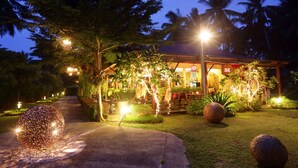 Un espacio exterior bien iluminado con un camino que lleva a un edificio, rodeado de árboles y luces decorativas.
