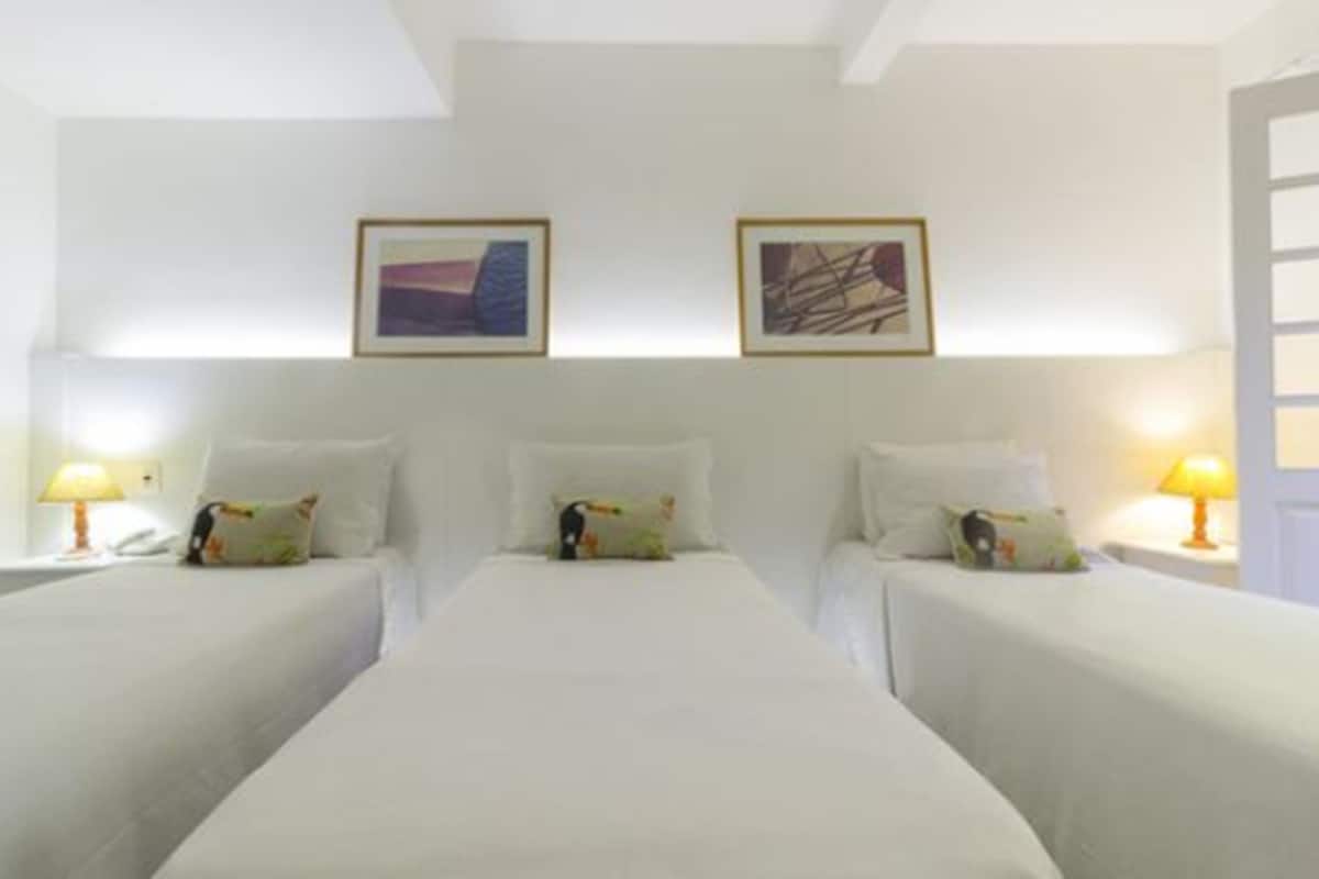 A hotel room with two beds, white bedding, and two bedside lamps. There are two framed artworks on the wall above the beds.