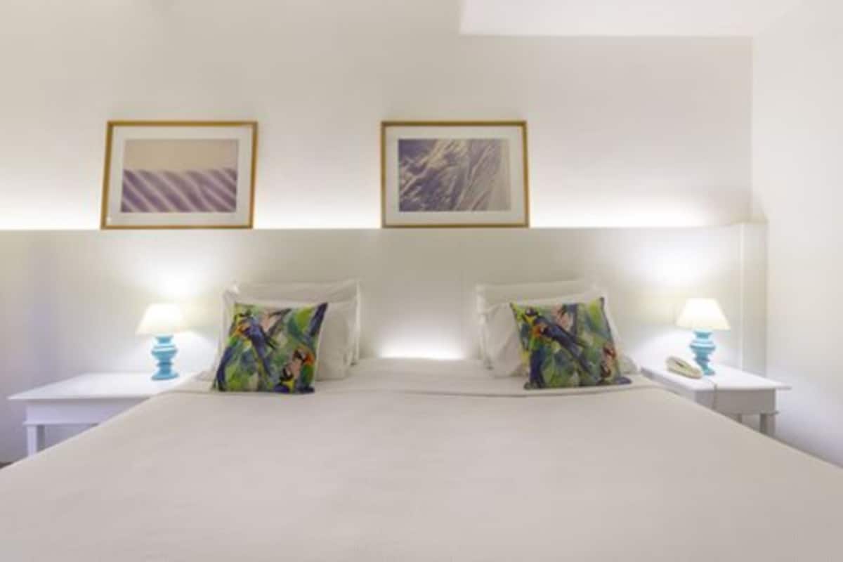 A hotel room with a large bed, two bedside tables with lamps, and two framed pictures on the wall.