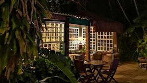 A cozy outdoor seating area with a table and chairs, surrounded by lush greenery and palm trees. - Pousada do Principe (Paraty)
