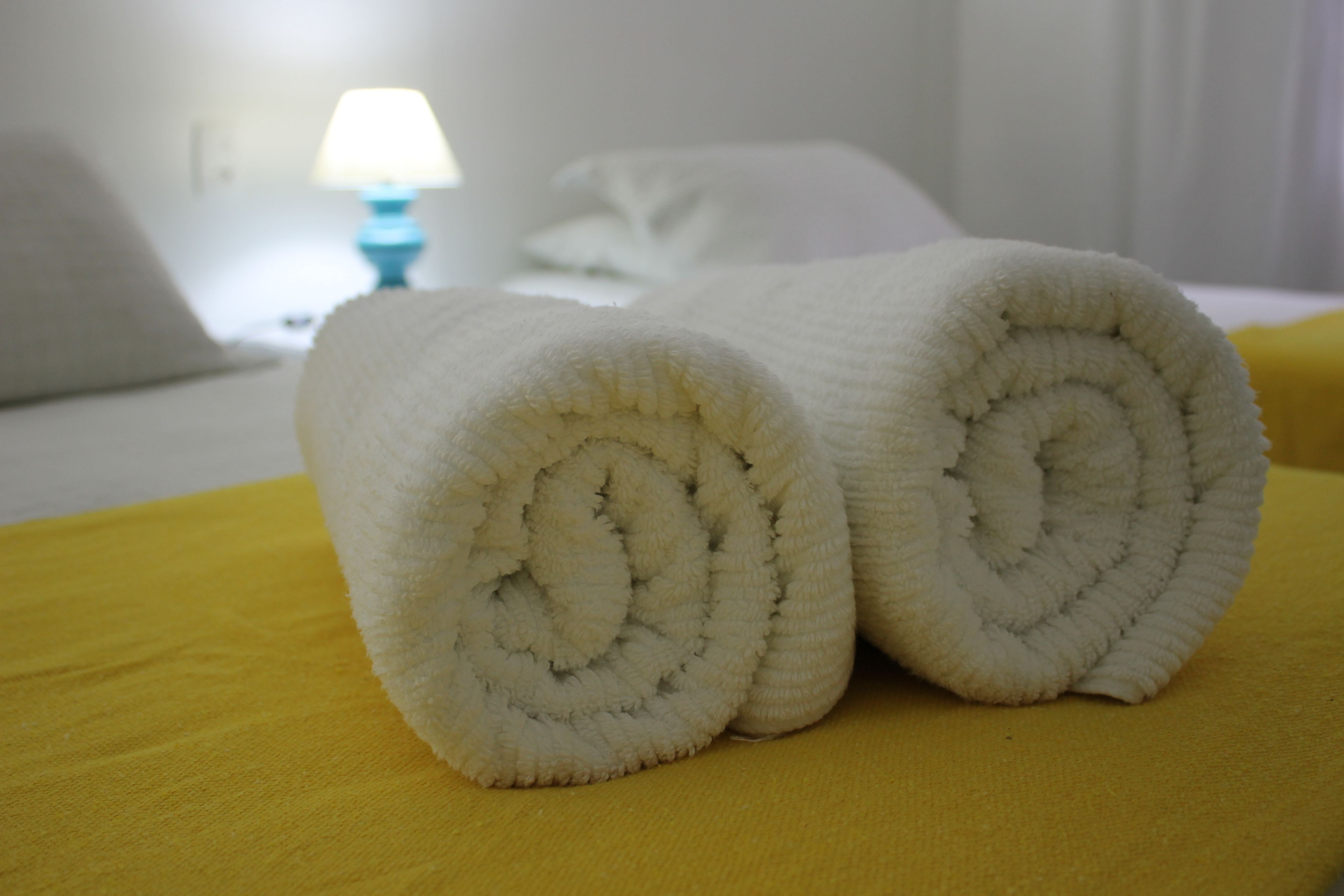 Zwei aufgerollte weiße Handtücher auf einer gelben Hoteldecke.