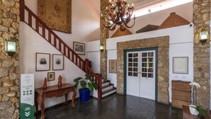 A grand staircase with a wooden handrail, a chandelier, stone walls, and a door with glass panels. - Pousada do Principe (Paraty)