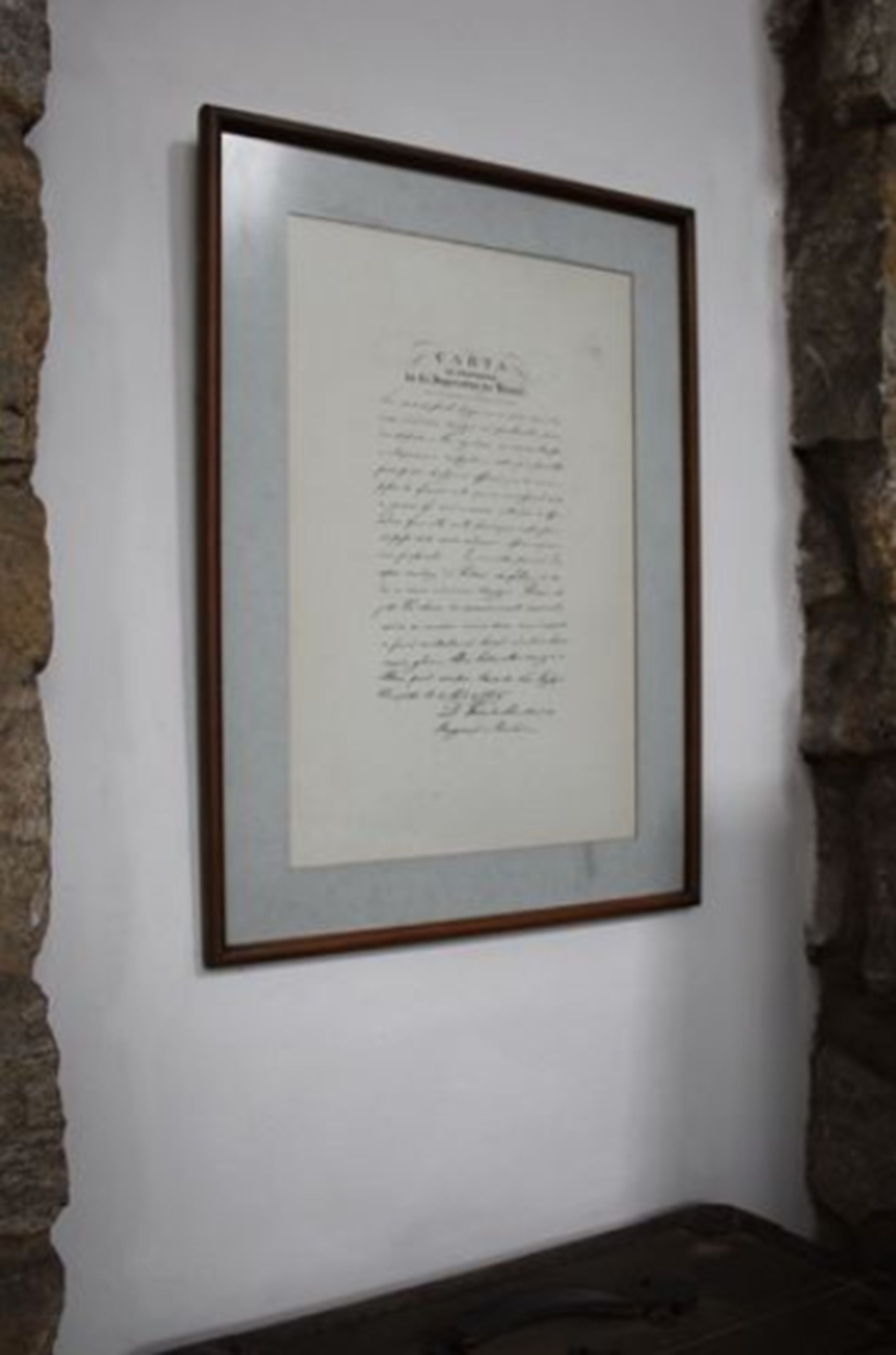 Un documento enmarcado en una pared, sobre un fondo de pared de piedra.