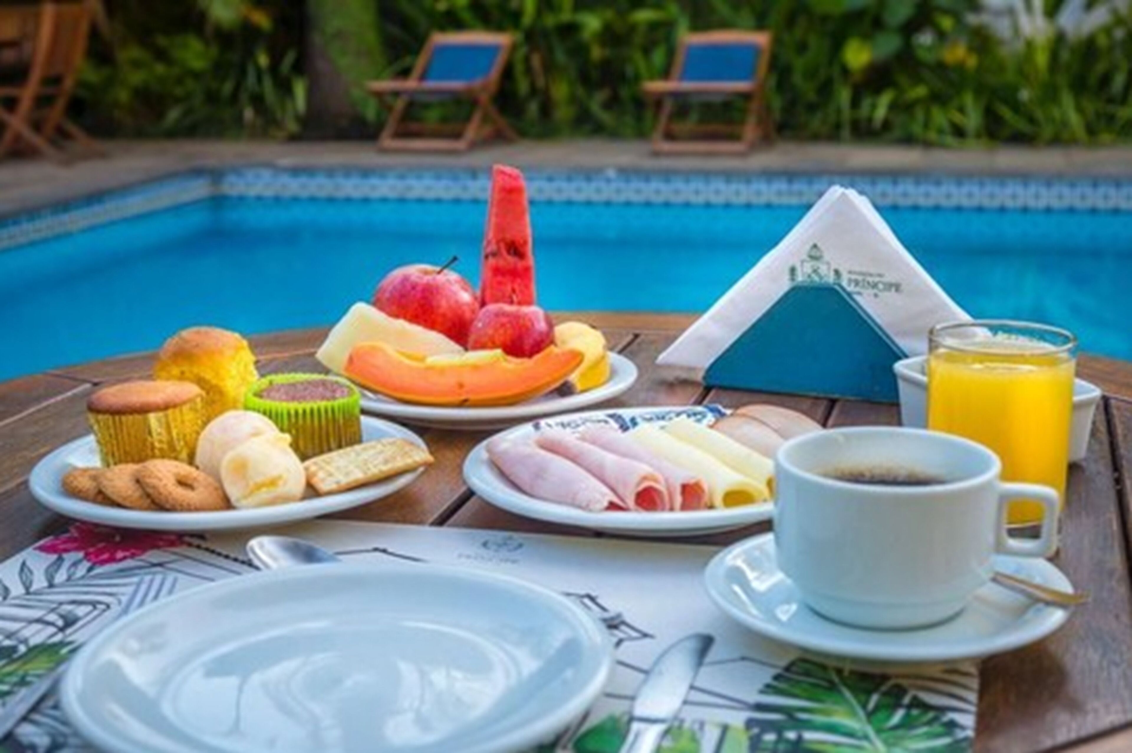 Een ontbijt bij het zwembad, met schalen fruit, gebak en een kop koffie.