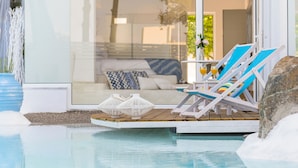 A modern outdoor pool area with lounge chairs and a glass-enclosed patio. - Kouros Home Hotel (Rhodes)