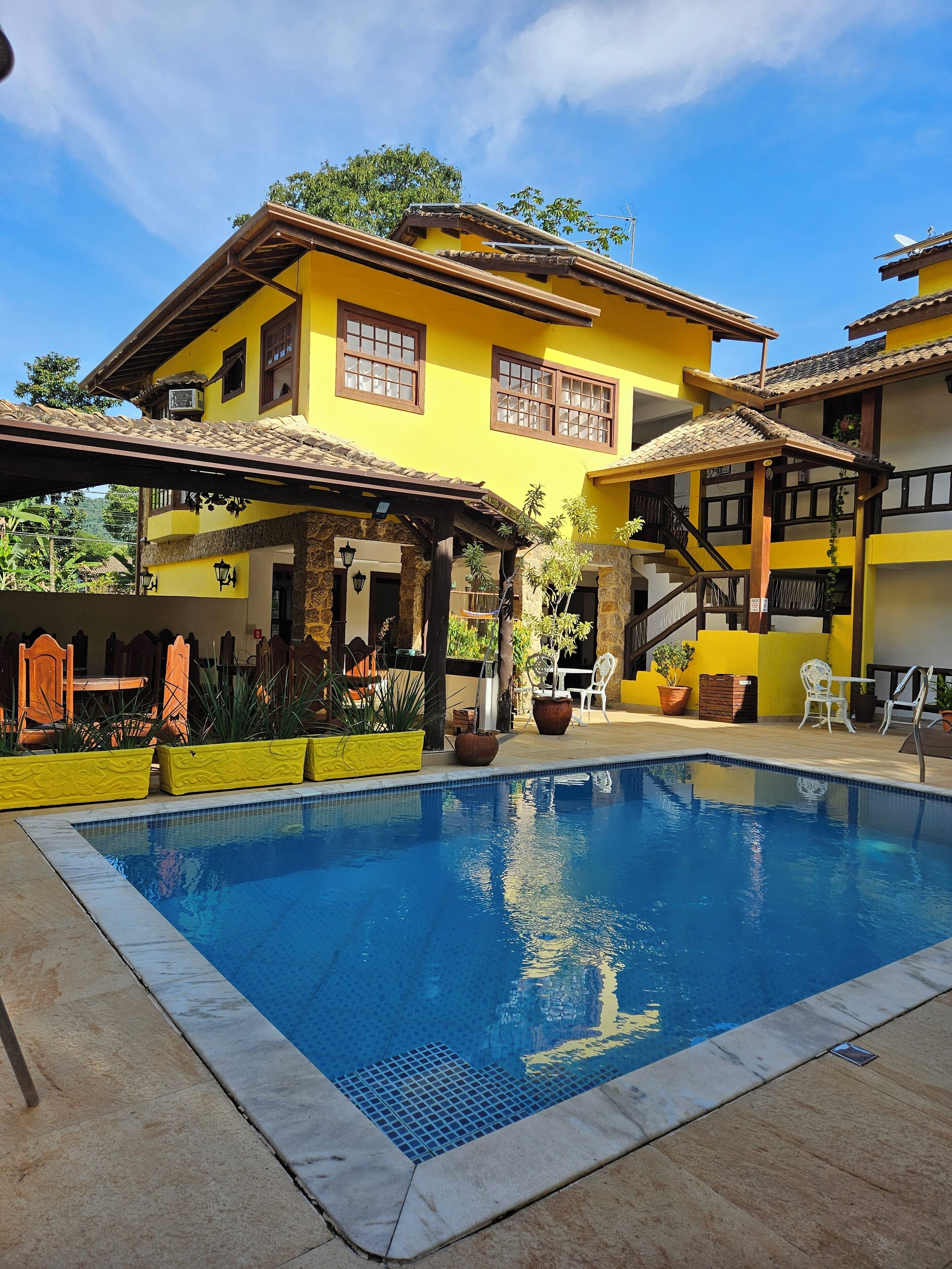A yellow building with a swimming pool, outdoor seating, and a covered patio area.