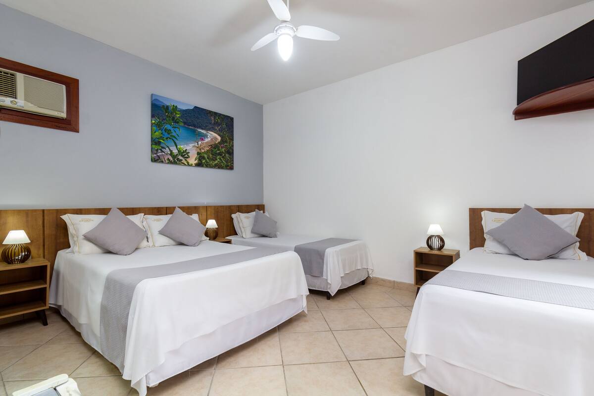 A hotel room with two beds, a ceiling fan, a painting, a TV, and a window with curtains.