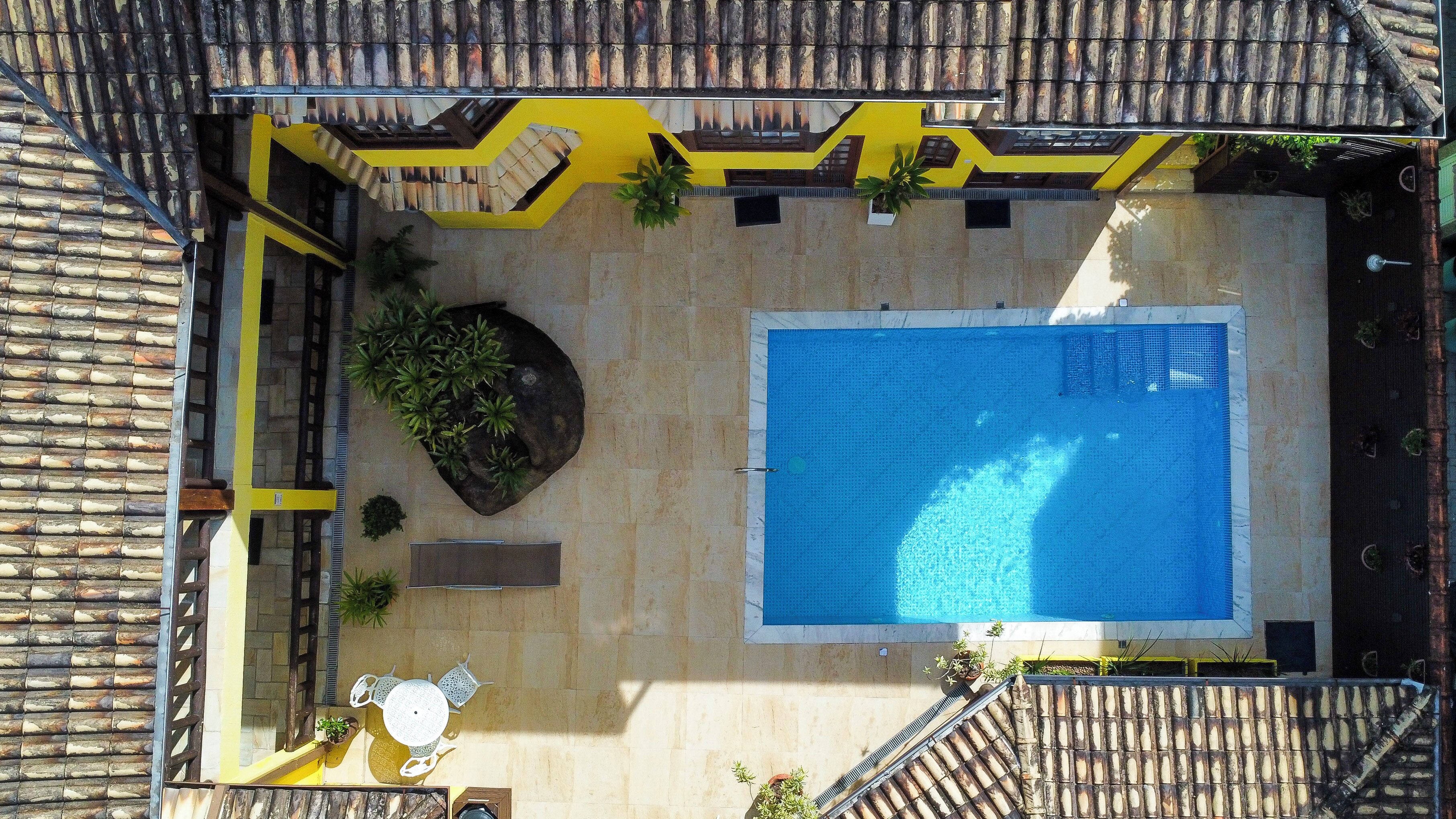 Vue aérienne d’une cour avec une piscine, des murs jaunes et blancs et un toit recouvert de tuiles.