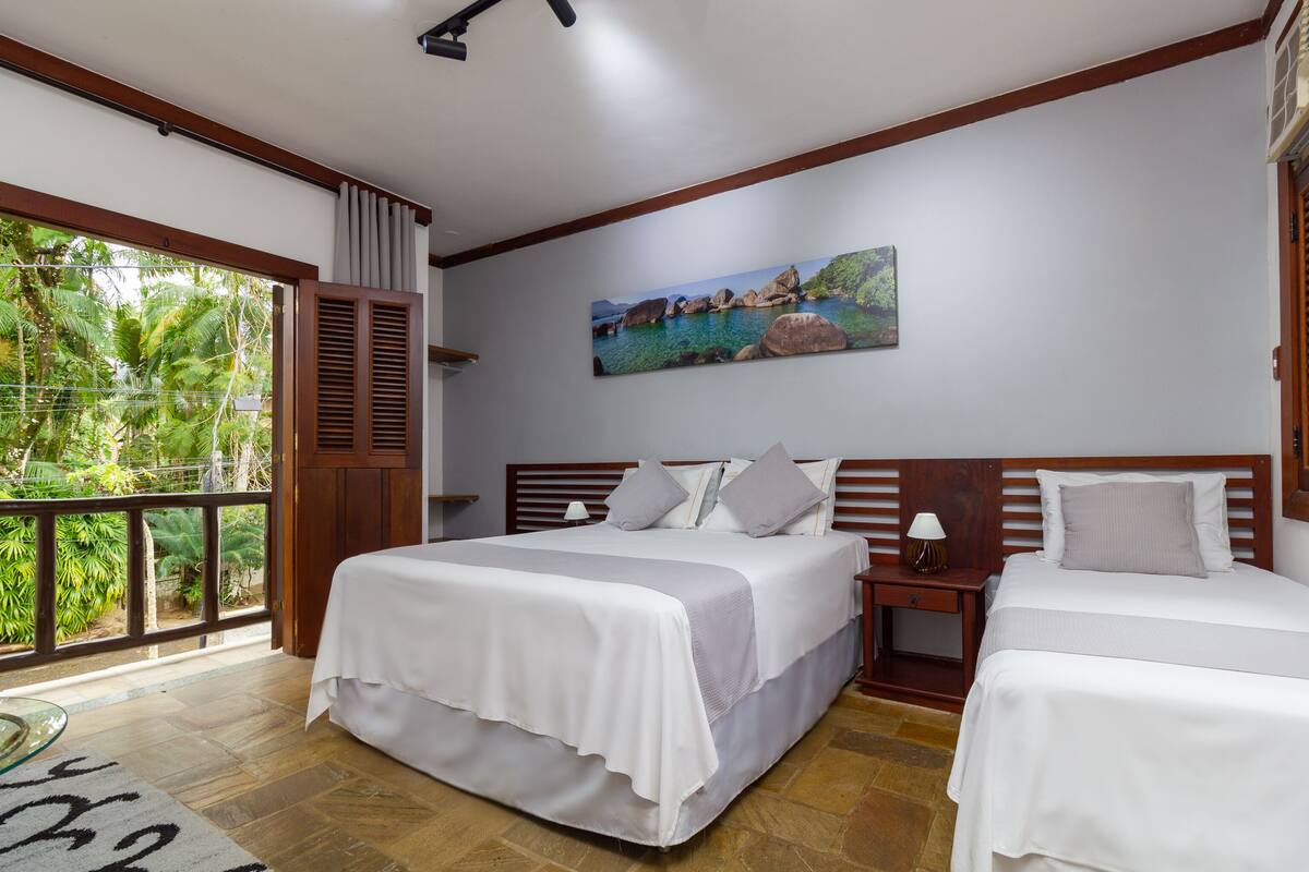 A bedroom with a large bed, a smaller bed, a nightstand, a lamp, and a painting of a coastal scene.