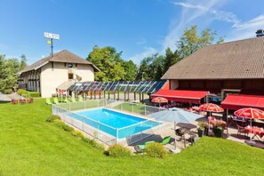 A swimming pool surrounded by a covered patio area with outdoor seating and umbrellas. - Alb'hotel Grill (Alby-sur-Cheran)