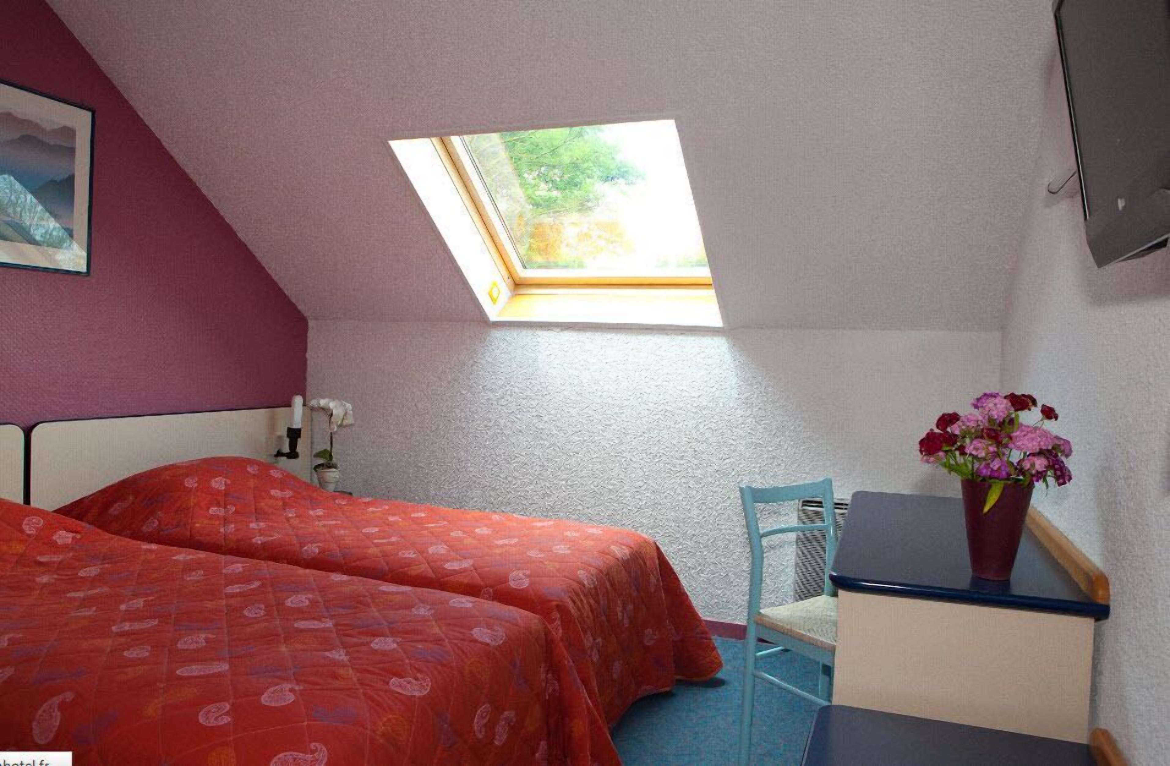 Ein Schlafzimmer mit zwei Betten, einem Oberlicht, einem Schreibtisch, einem Stuhl und einer Zimmerpflanze.