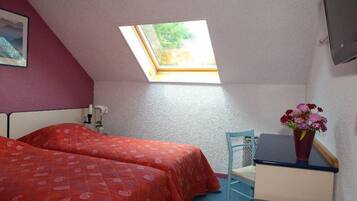 Ein Schlafzimmer mit zwei Betten, einem Oberlicht, einem Schreibtisch, einem Stuhl und einer Zimmerpflanze.