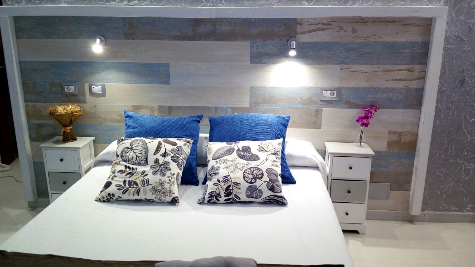 A modern bedroom with a bed, two nightstands, and a decorative wall.