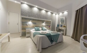 A modern bedroom with a large bed, bedside tables, a vanity with a mirror, and a door leading to another room. - Hotel Sun Holidays (Puerto de la Cruz)