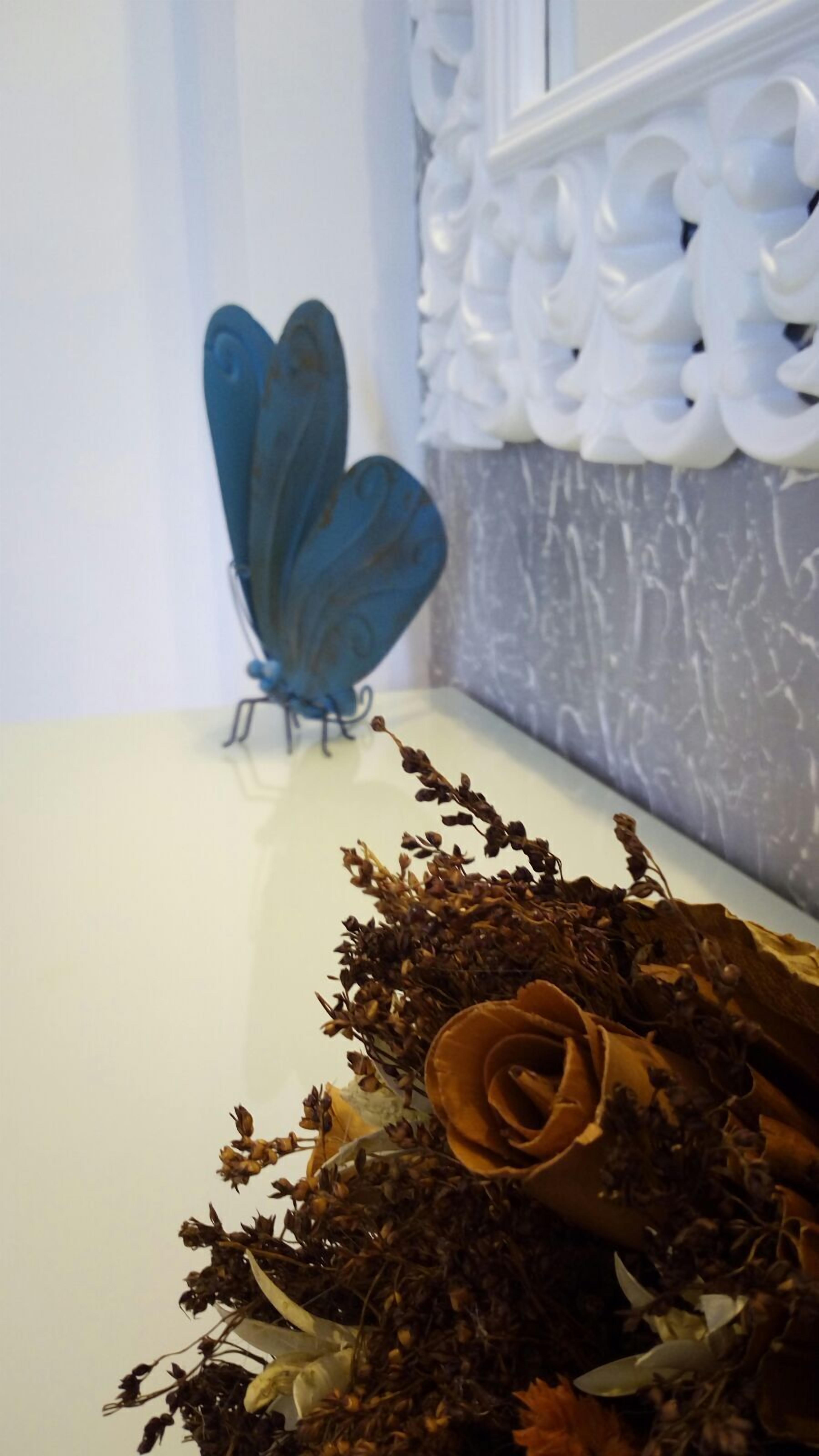 A decorative blue butterfly on a white surface, surrounded by dried flowers and a rose.