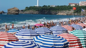 A beach with striped umbrellas, a lighthouse, and rocky cliffs.