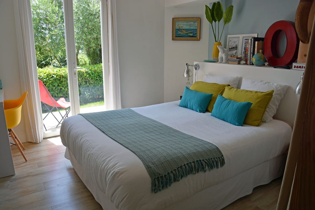 A bedroom with a large bed, a chair, and a view of the outdoors.