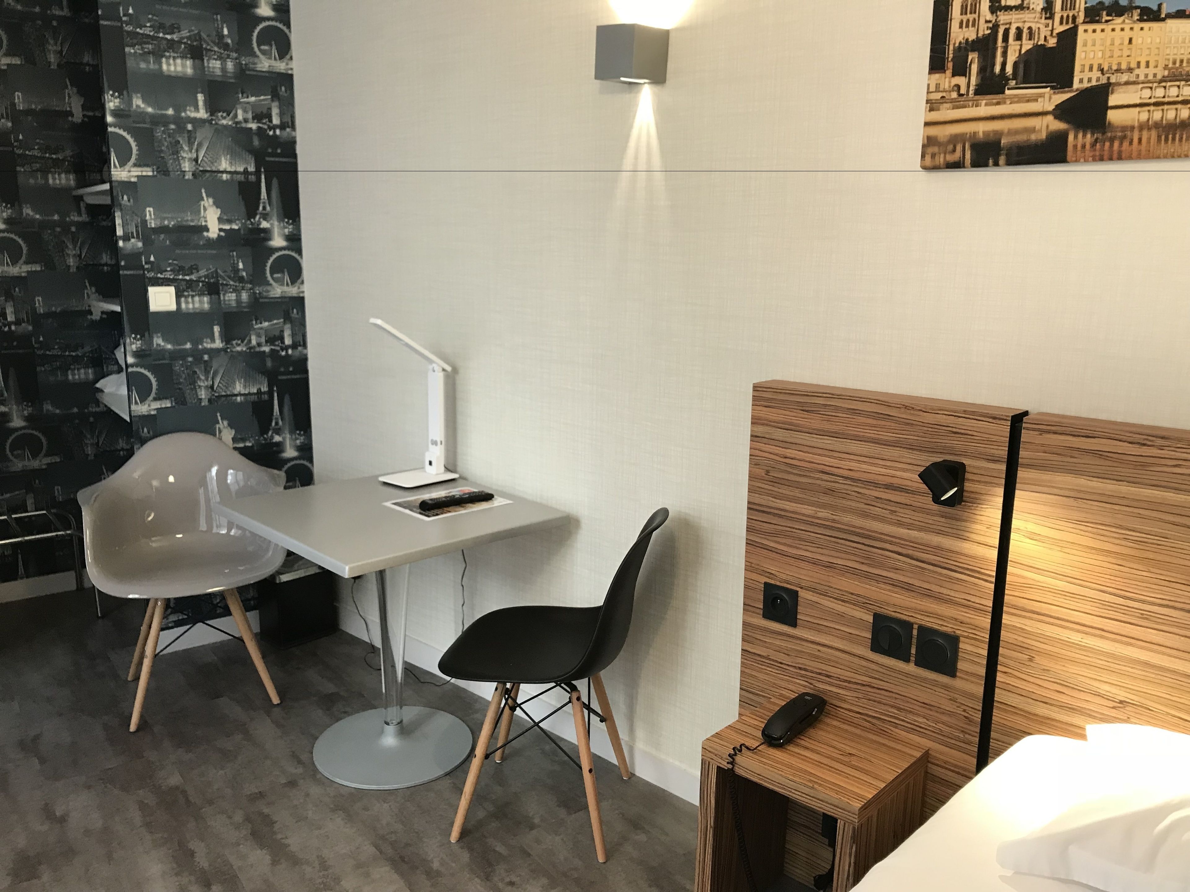 Una habitación de hotel moderna con cabecera de madera, un escritorio con silla, una lámpara de pie y una luz de pared.
