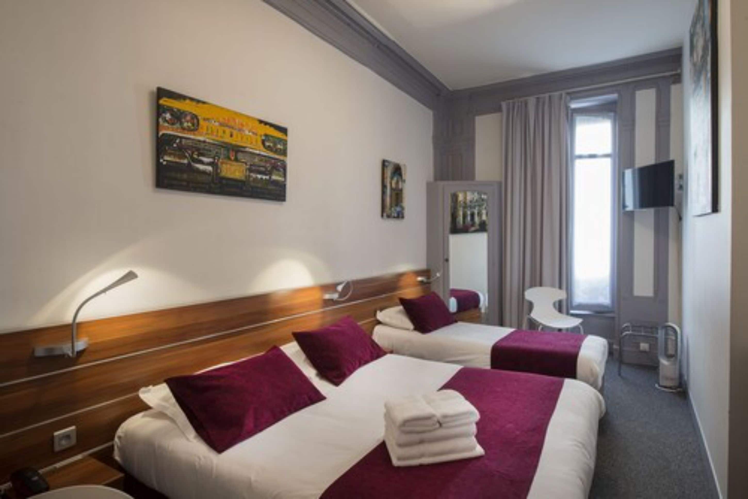 Habitación de hotel con dos camas, un escritorio, una silla, un televisor y una ventana con cortinas.