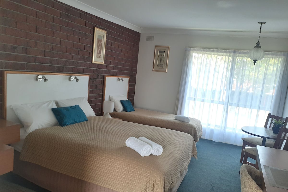 A hotel room with two beds, a dining table, and a large window with curtains.