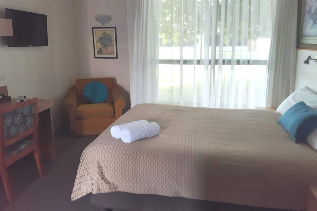 A hotel room with a bed, a chair, a desk, and a TV mounted on the wall.