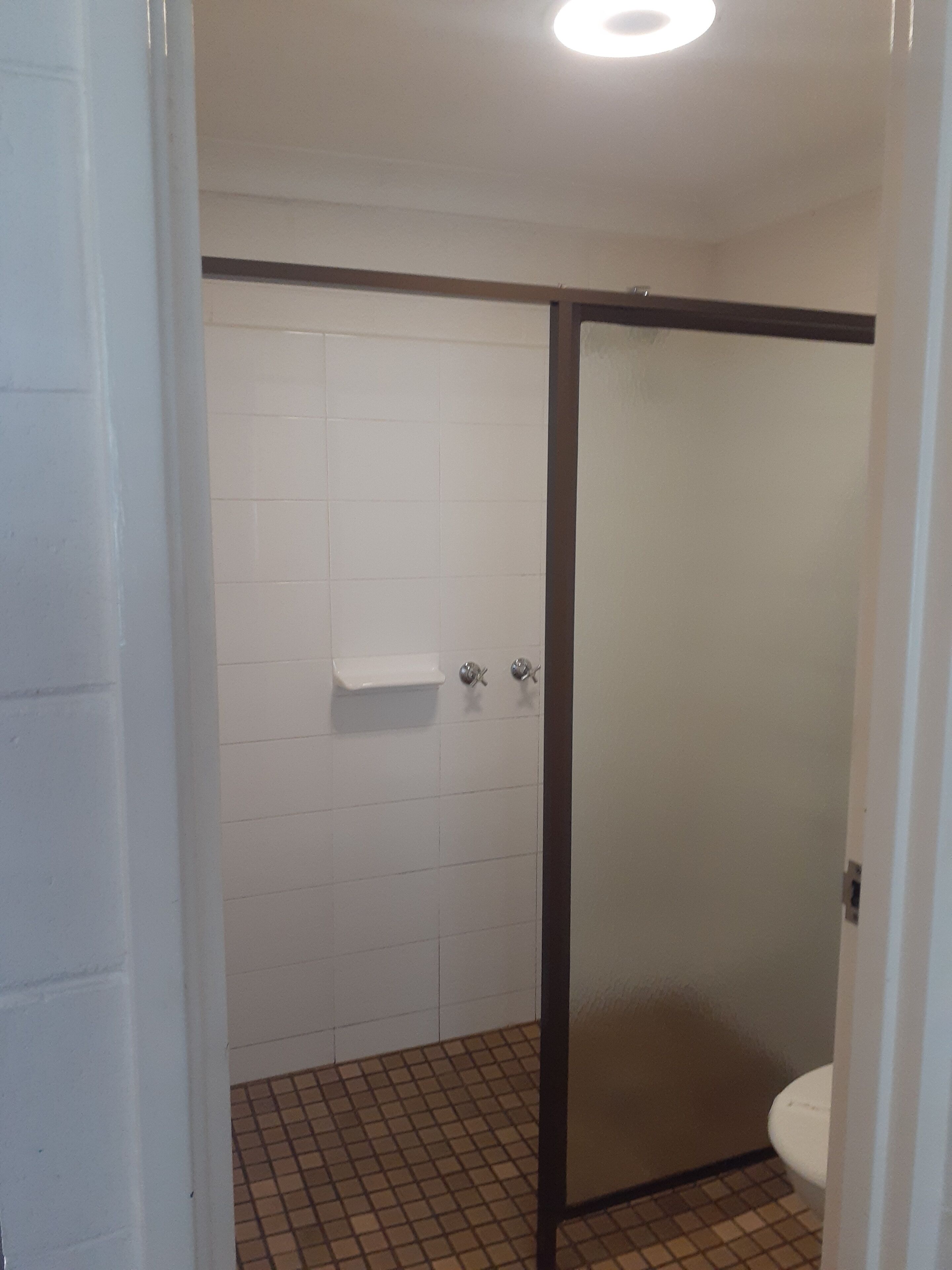 A bathroom with white tiled walls, a shower with a glass door, and a toilet.