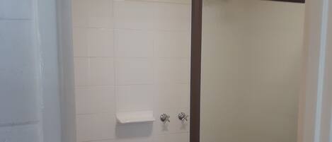 A bathroom with white tiled walls, a shower with a glass door, and a toilet.