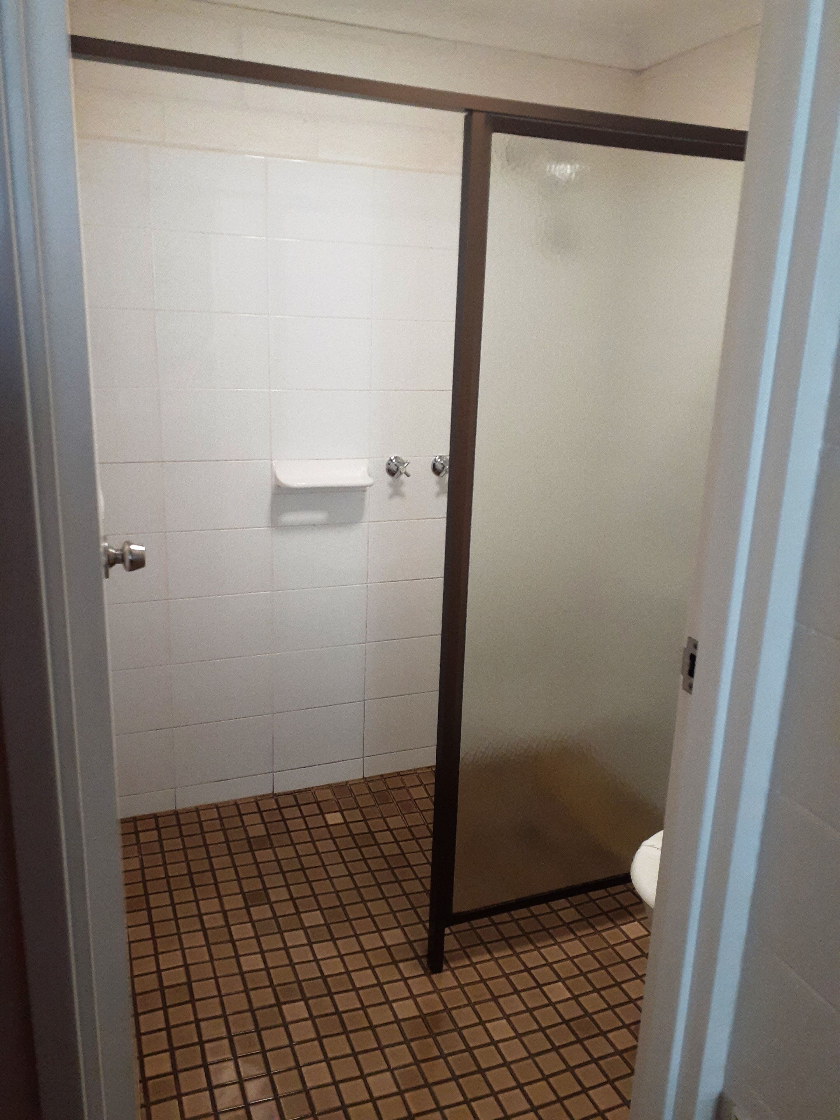 Un baño con paredes de azulejos blancos, cabina de ducha con puerta de vidrio esmerilado y piso de azulejos.