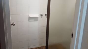 Een badkamer met witte betegelde wanden, een douchecabine met een matglazen deur en een betegelde vloer.