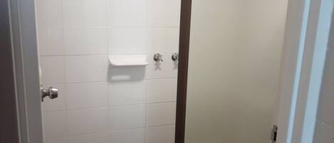 Un baño con paredes de azulejos blancos, cabina de ducha con puerta de vidrio esmerilado y piso de azulejos.