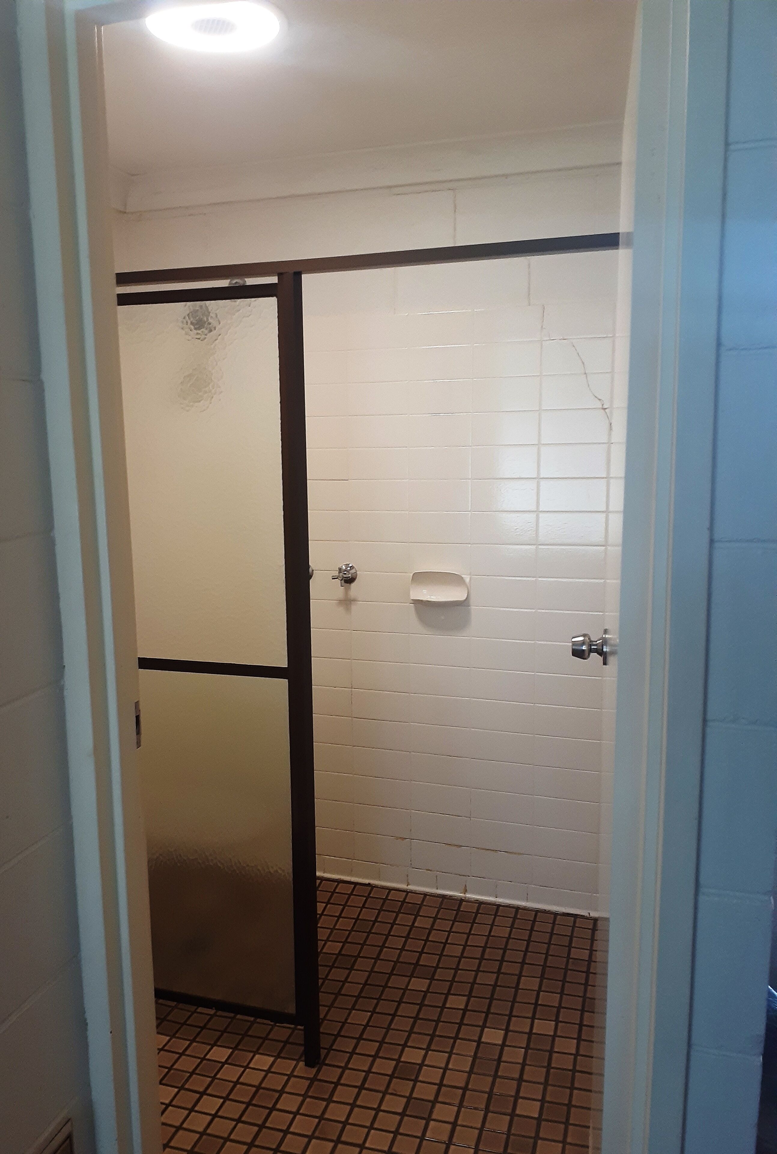 Un baño con paredes de azulejos blancos, una puerta con marco negro, un pequeño jabonera blanca y suelo de azulejos.