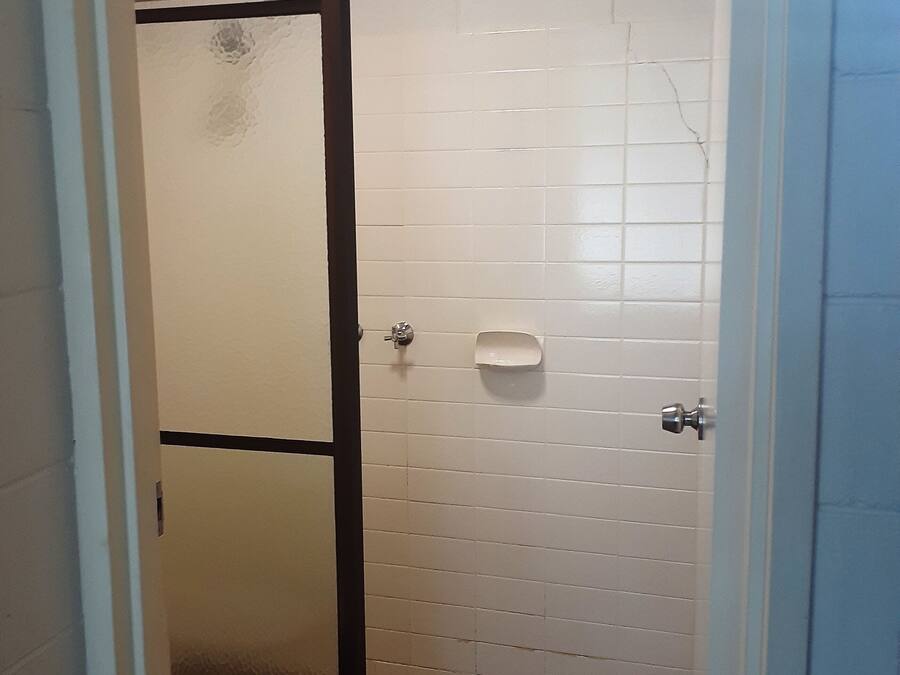 Un baño con paredes de azulejos blancos, una puerta con marco negro, un pequeño jabonera blanca y suelo de azulejos.