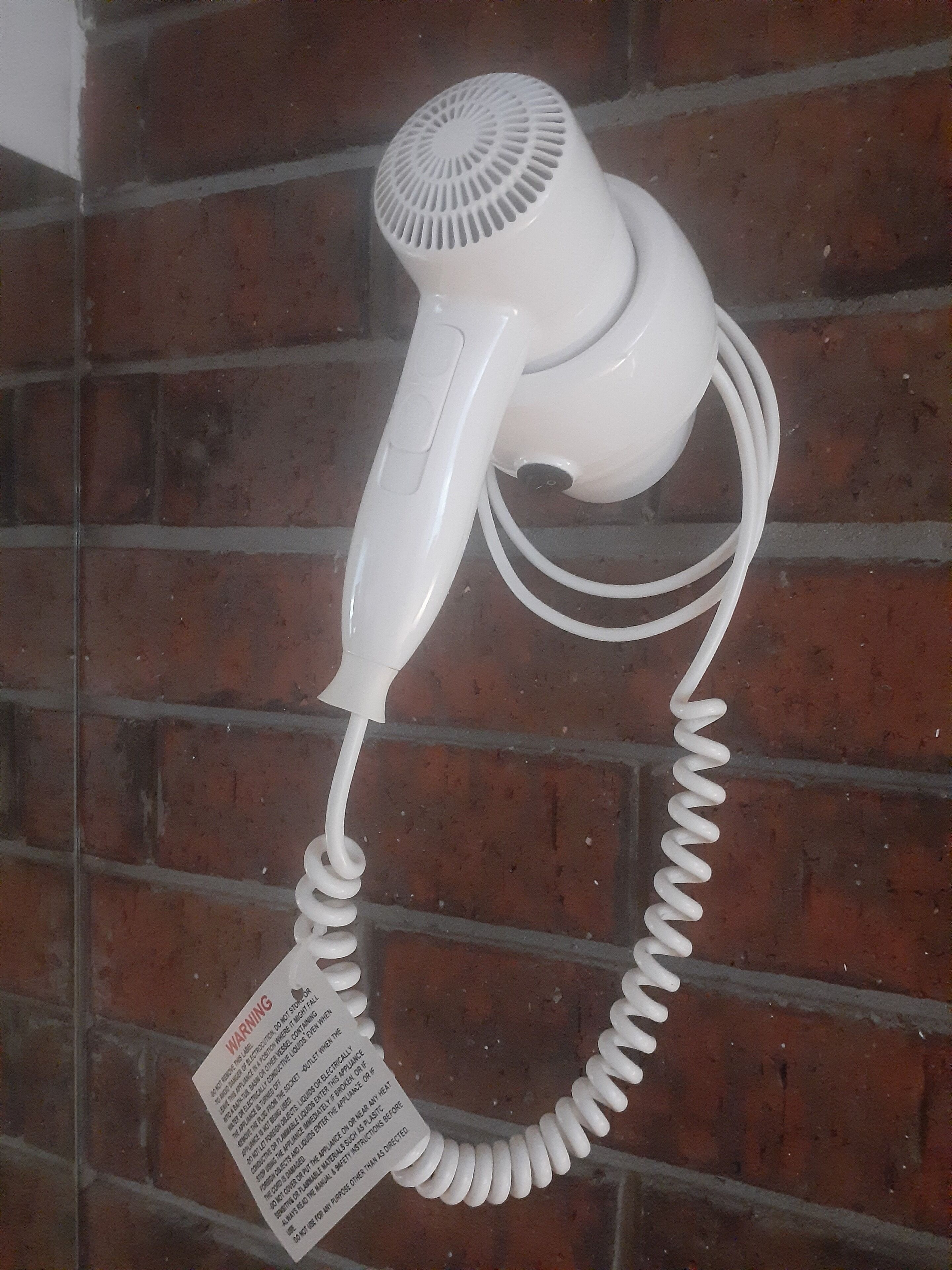 A white hair dryer mounted on a brick wall.