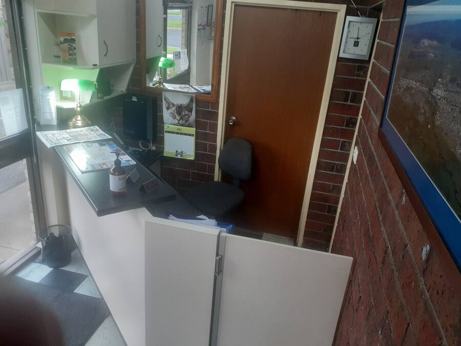 A small office with a desk, chair, and a door. There is a window with a view of the outside, a clock on the wall, and a calendar on the door.