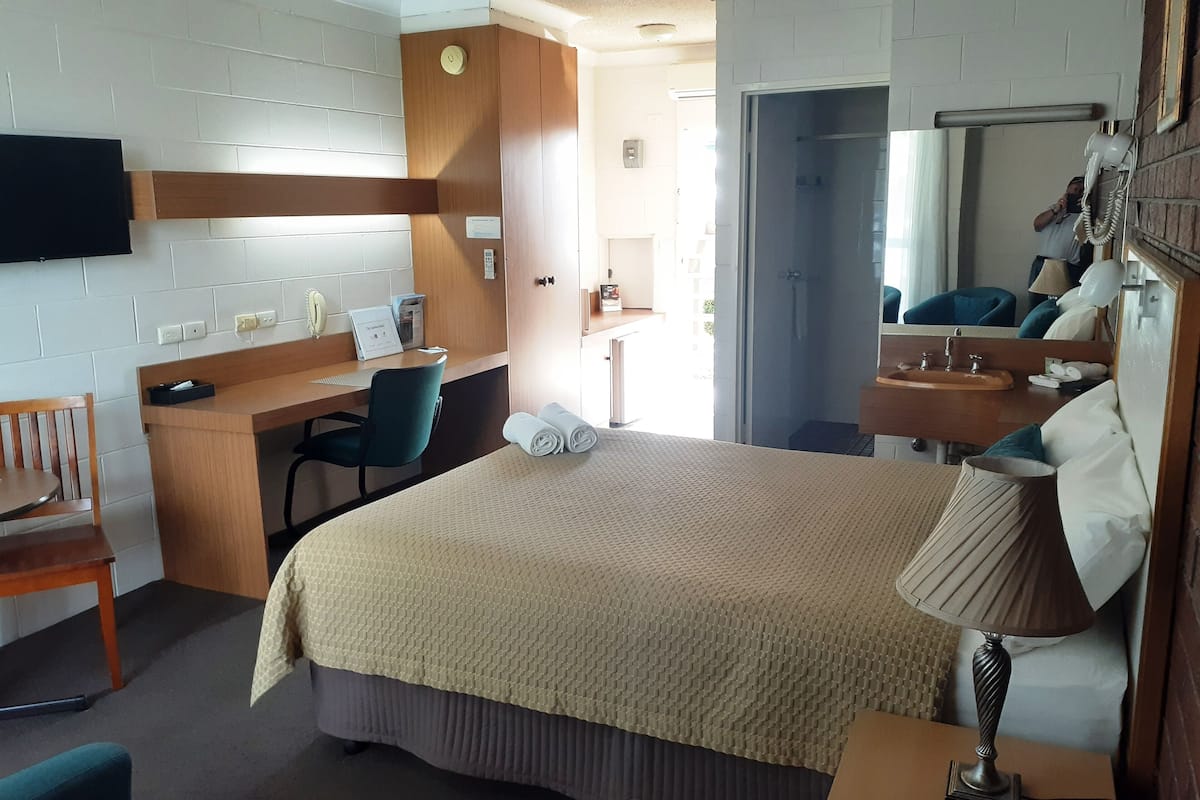 A hotel room with a bed, desk, chair, and a bathroom with a sink and mirror.