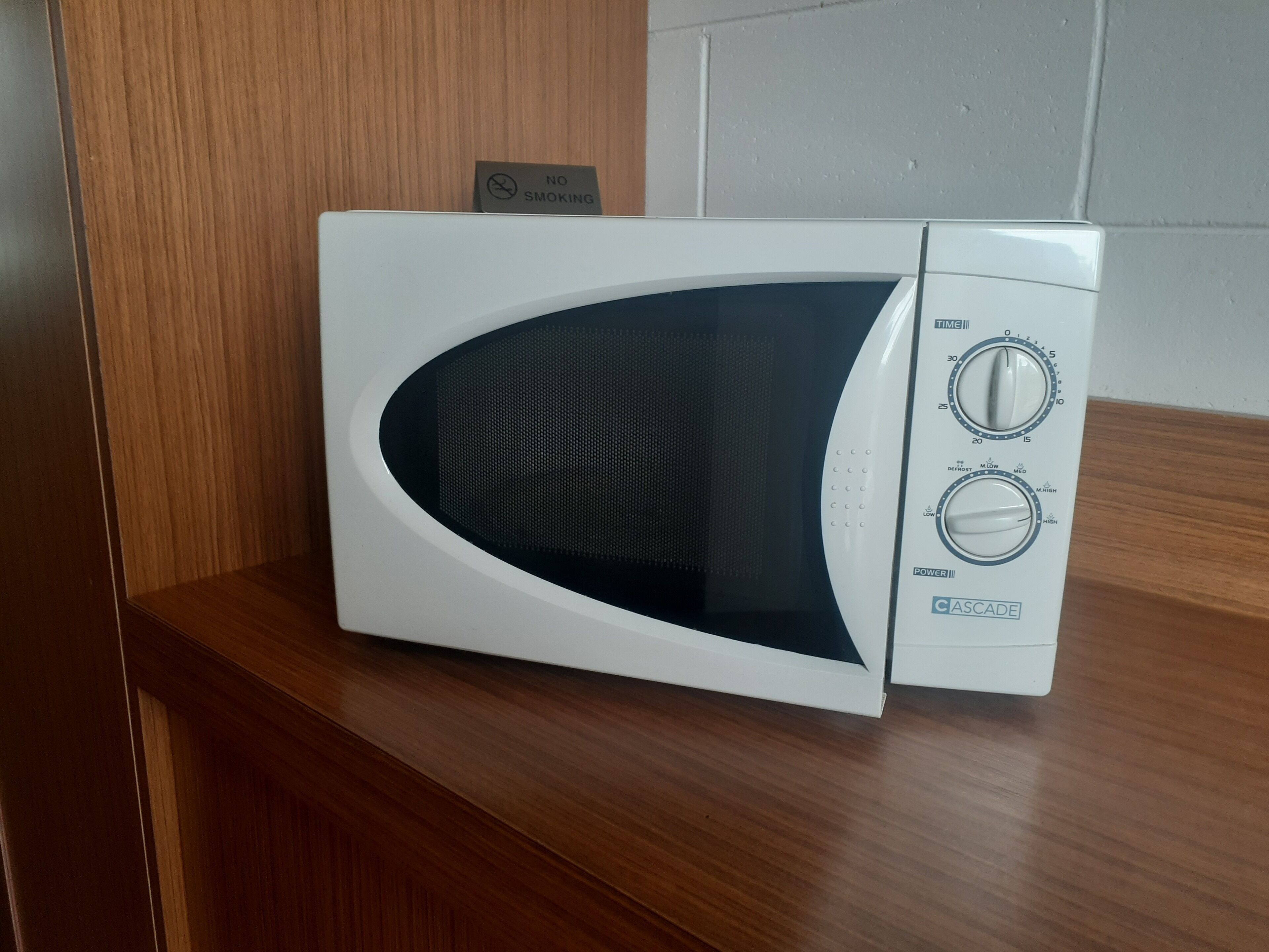 Un horno microondas blanco con perillas de control y un temporizador en el lado derecho, sobre una encimera de madera.